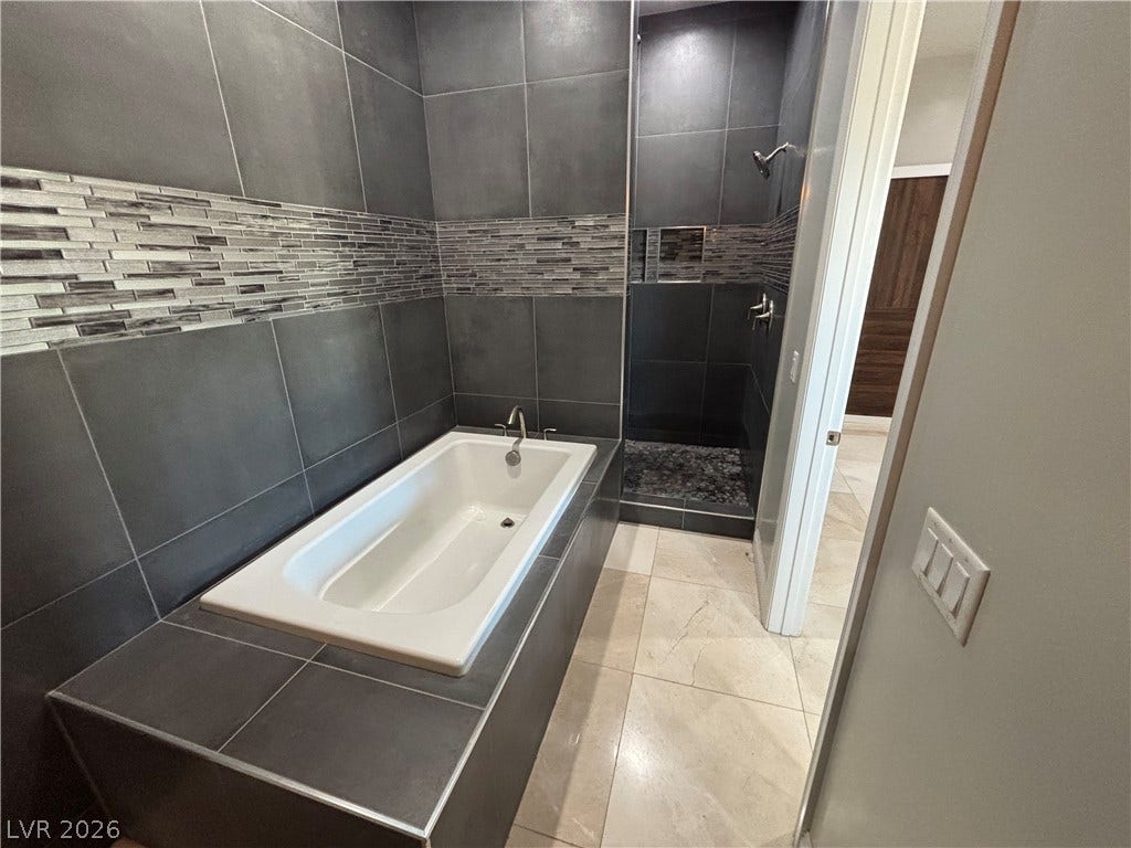 Dark tiling surrounds a built-in soaking tub alongside a separate walk-in shower.