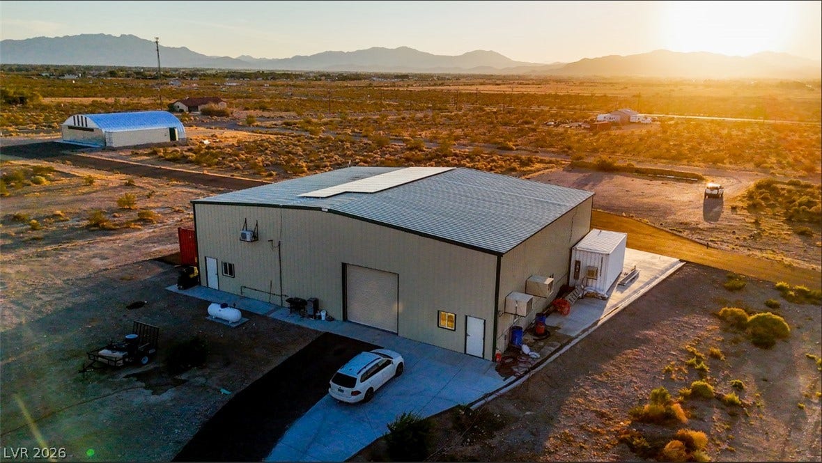 An expansive metal outbuilding stands against a backdrop of distant mountains at sunset.