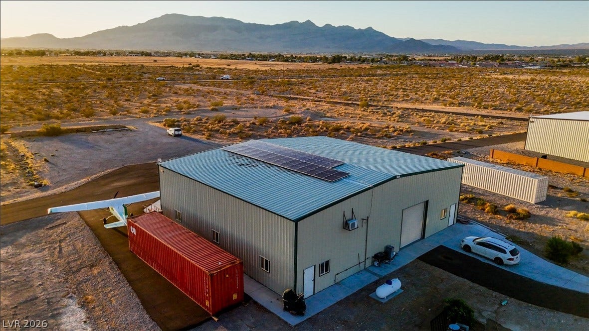 A spacious metal hangar with solar panels sits against a dramatic mountain backdrop.