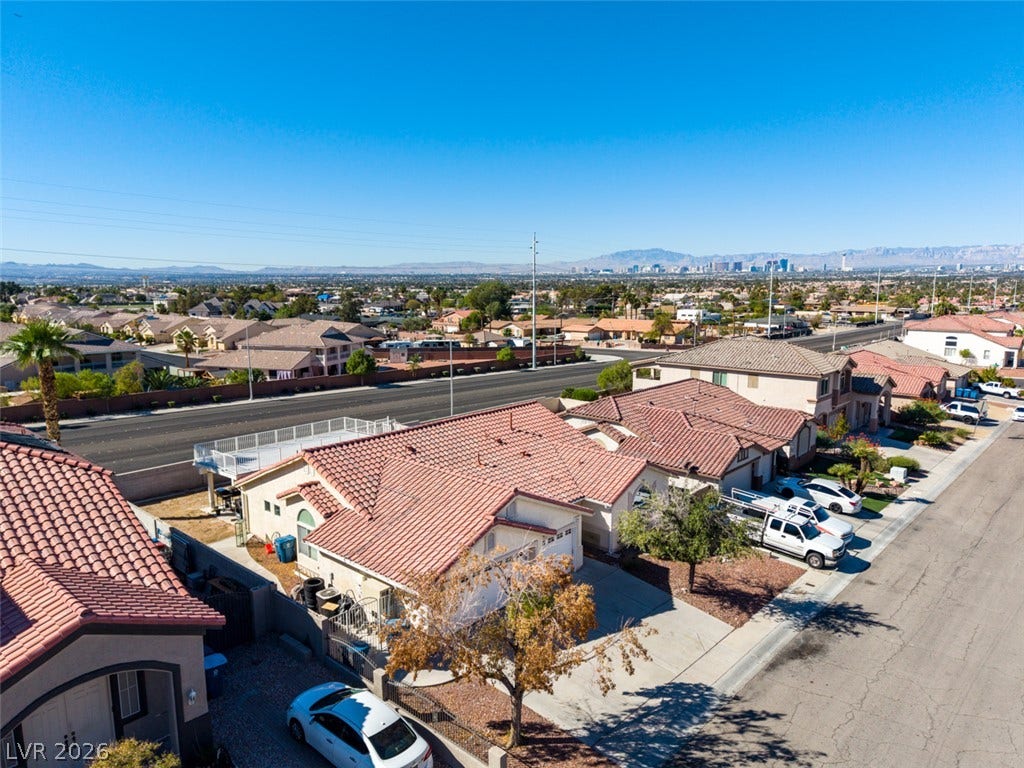 6543 Mahogany Peak Avenue, Las Vegas, NV 89110 Tiled roofs frame a suburban neighborhood overlooking distant mountains and a city skyline.