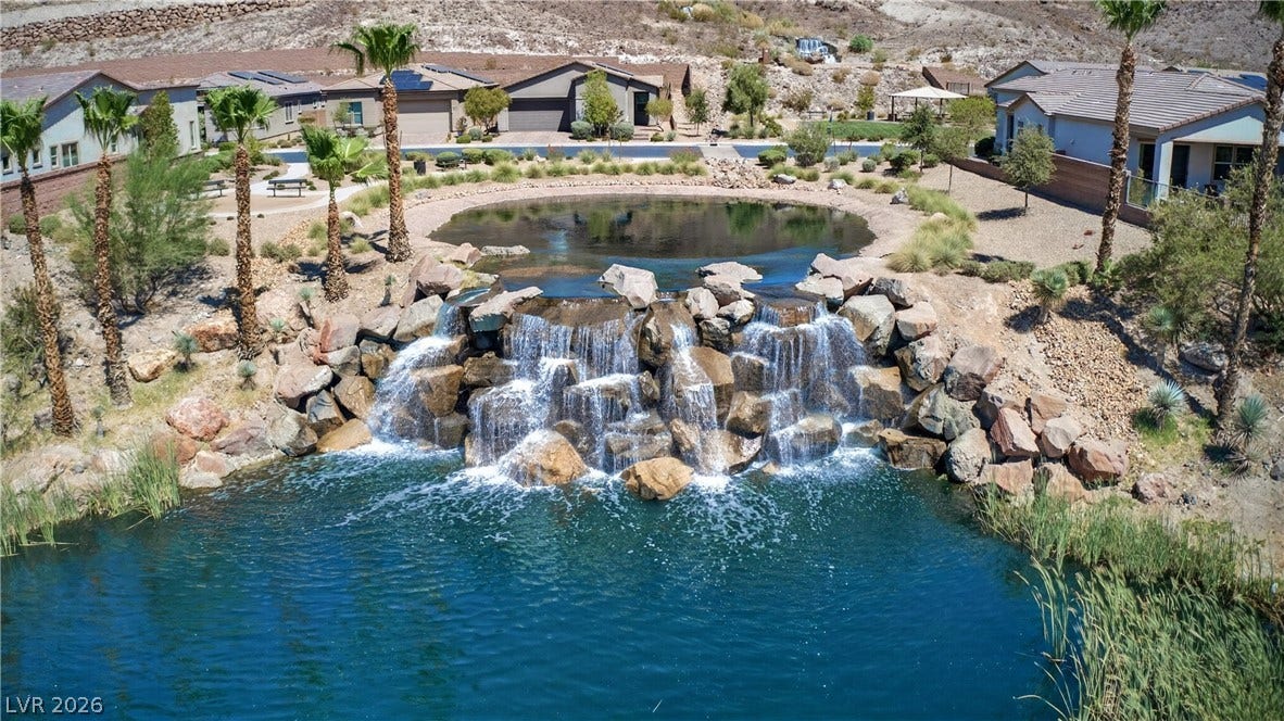 4 Bobado Lane, Henderson, NV 89011 An cascading rock waterfall flows into a tranquil blue pond surrounded by palm trees.