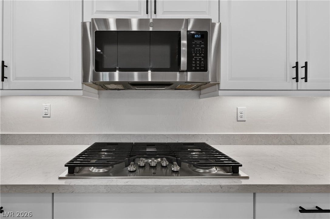4 Bobado Lane, Henderson, NV 89011 A modern gas cooktop integrates seamlessly beneath a built-in microwave and white shaker cabinetry.