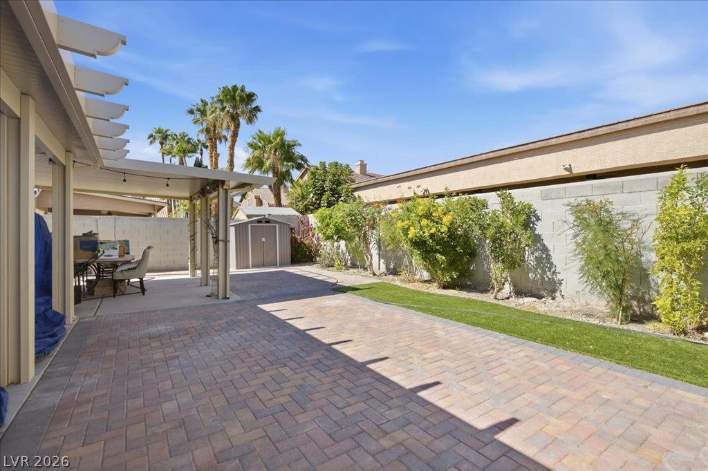 An inviting paved patio area is covered by a pergola alongside a tidy lawn.