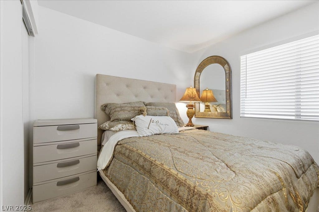 Plentiful natural light streams through a large window into this cozy carpeted bedroom.