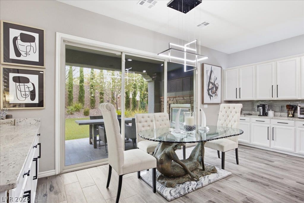 181 Elder View Drive, Las Vegas, NV 89138 A well-lit dining area featuring a unique glass-top table, seamlessly connected to a verdant outdoor space through large sliding glass doors.