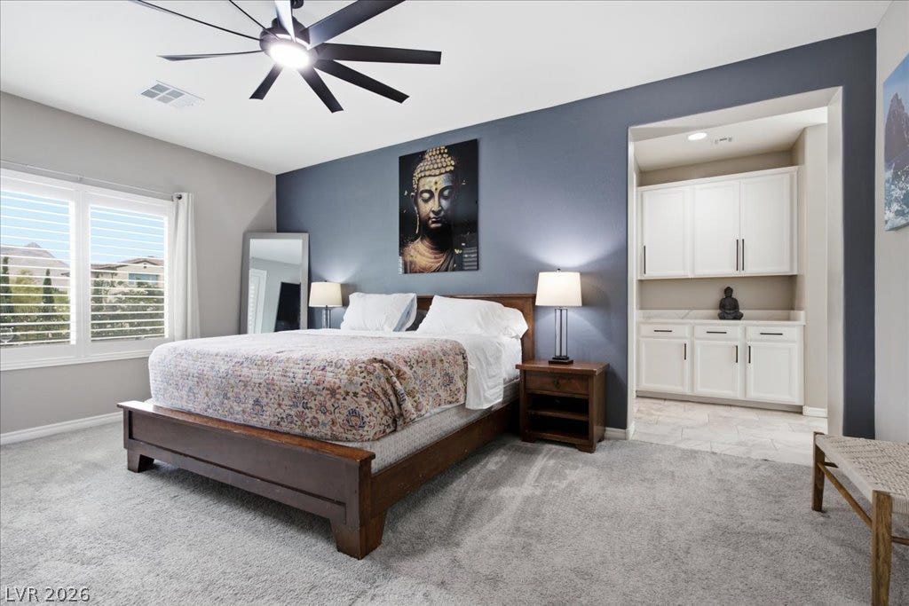 181 Elder View Drive, Las Vegas, NV 89138 Comfortable carpeted bedroom features a ceiling fan, dual windows with plantation shutters, and a convenient built-in dry bar.