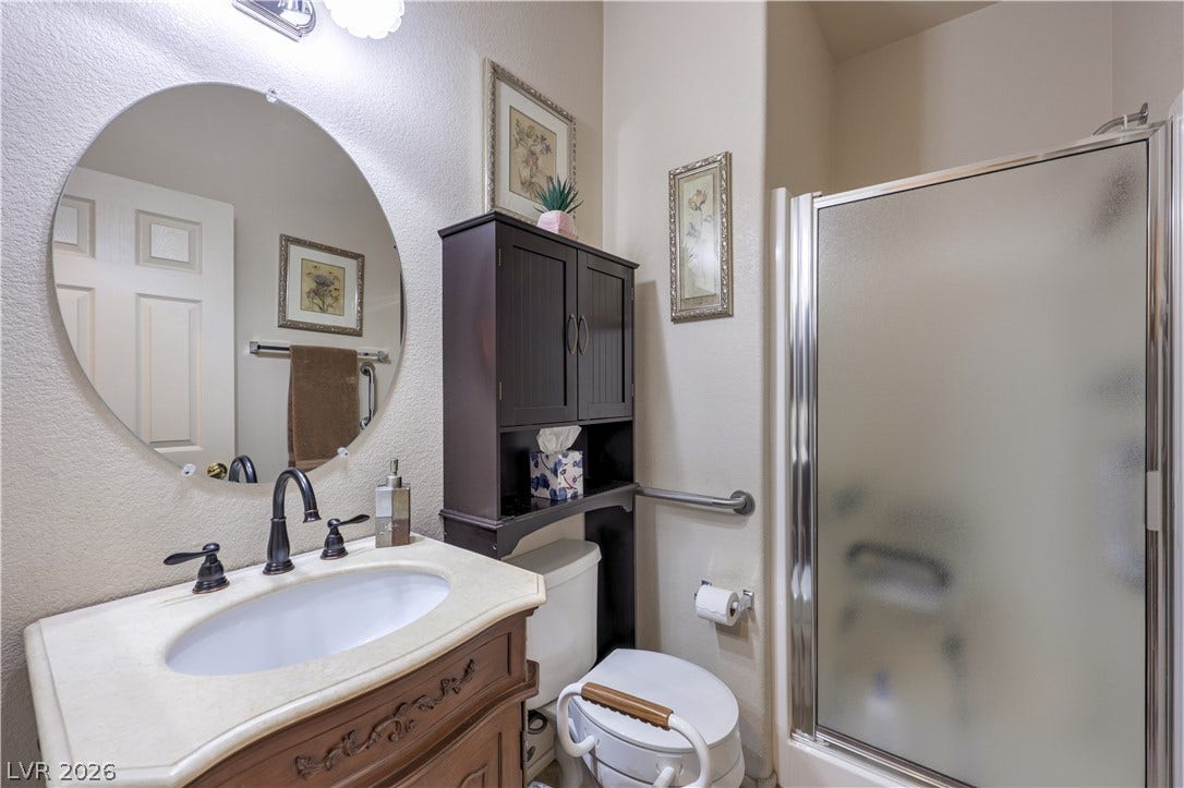 10474 Rustyville Court, Las Vegas, NV 89129 A well-appointed bathroom features a classic vanity, a circular mirror, and a convenient walk-in shower.