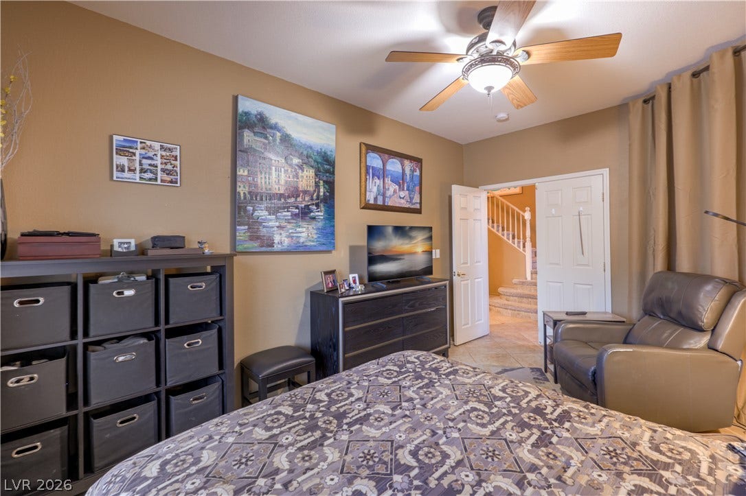 10474 Rustyville Court, Las Vegas, NV 89129 Relaxation awaits in this inviting bedroom with a cooling ceiling fan and convenient access to a private stairway.