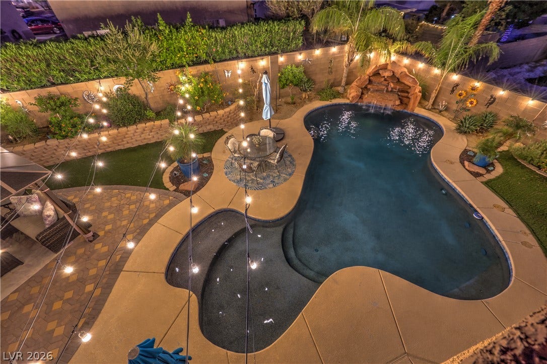 10474 Rustyville Court, Las Vegas, NV 89129 A private backyard oasis features a custom-shaped pool with a rock waterfall and integrated spa, perfect for evening relaxation.