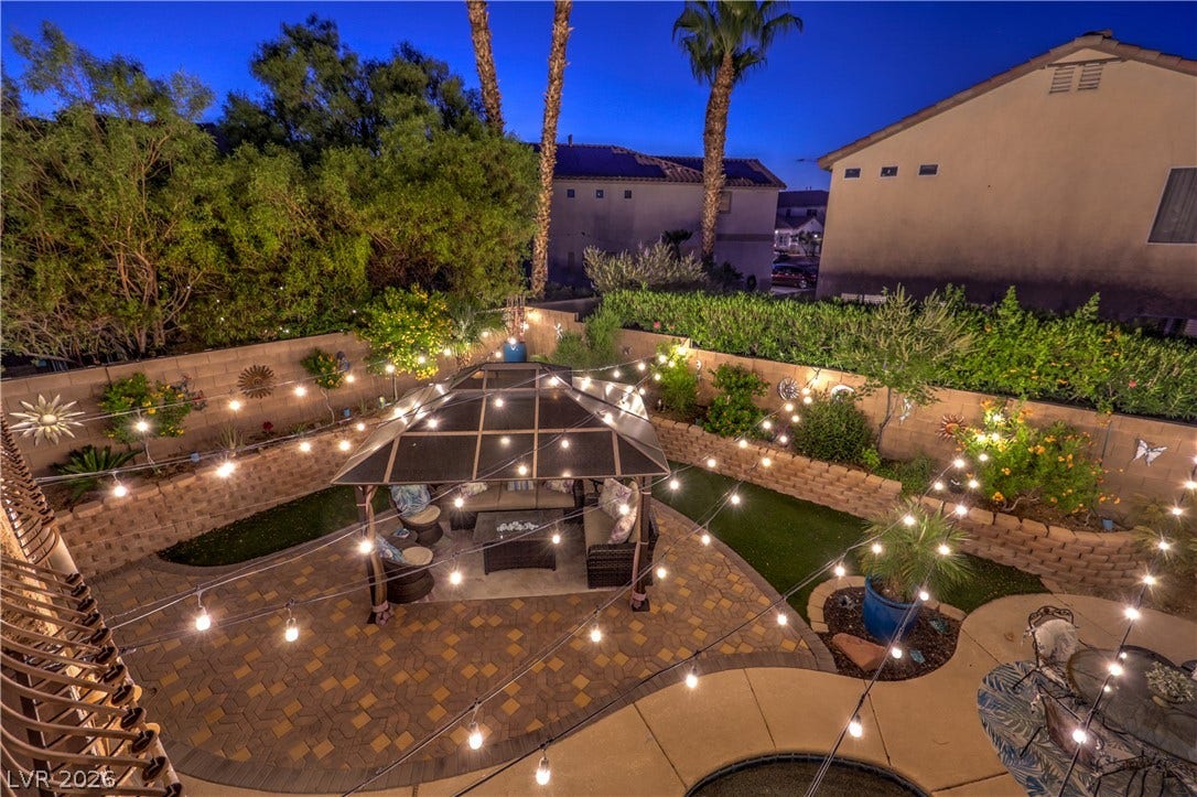 10474 Rustyville Court, Las Vegas, NV 89129 The backyard oasis features a paved patio, lush landscaping, and a cozy gazebo, all illuminated by enchanting string lights.
