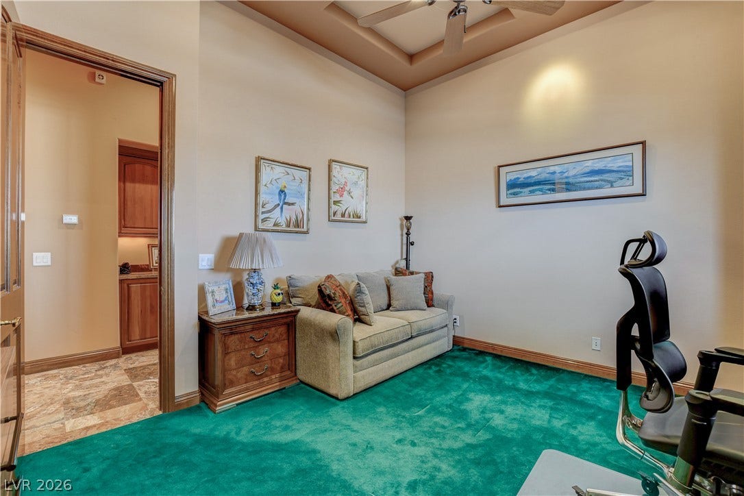 A spacious home office offers plush wall-to-wall carpeting and a dynamic tray ceiling.