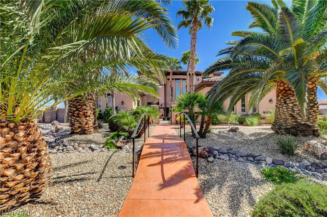 Mature palm trees and xeriscaped beds line a concrete path leading to the entrance.