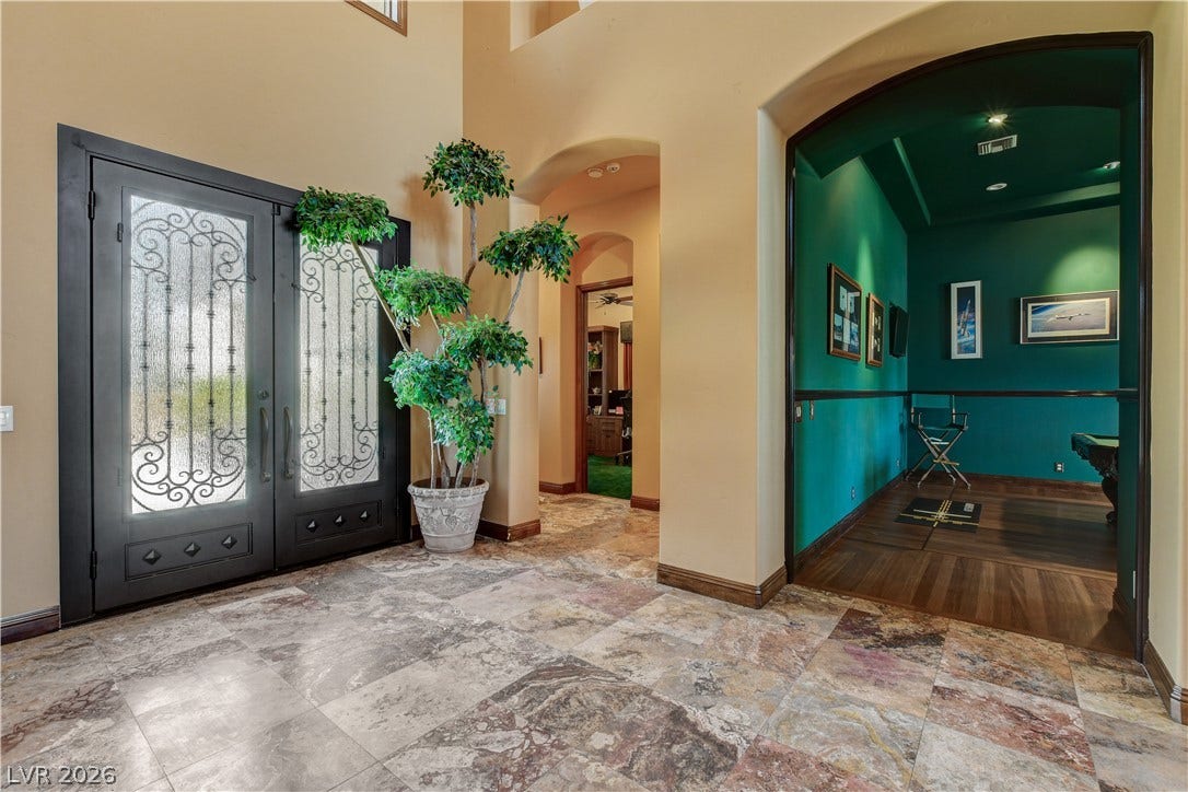 Ornate double doors open into a grand foyer featuring textured tile flooring and arched transitions.
