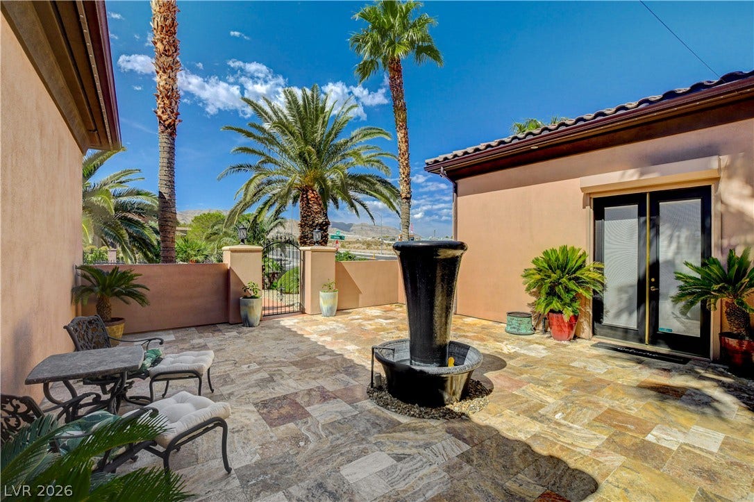 An inviting stone-tiled courtyard features a central fountain under towering palm trees.
