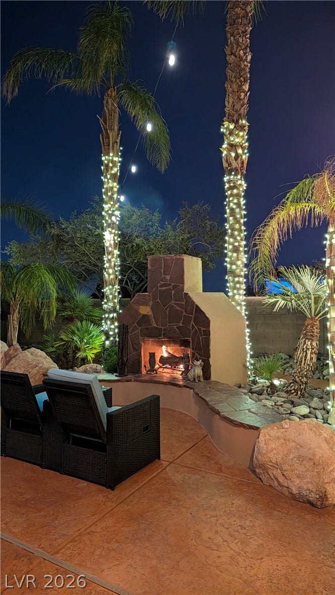 An outdoor stone fireplace anchors the stamped concrete patio under towering palm trees.