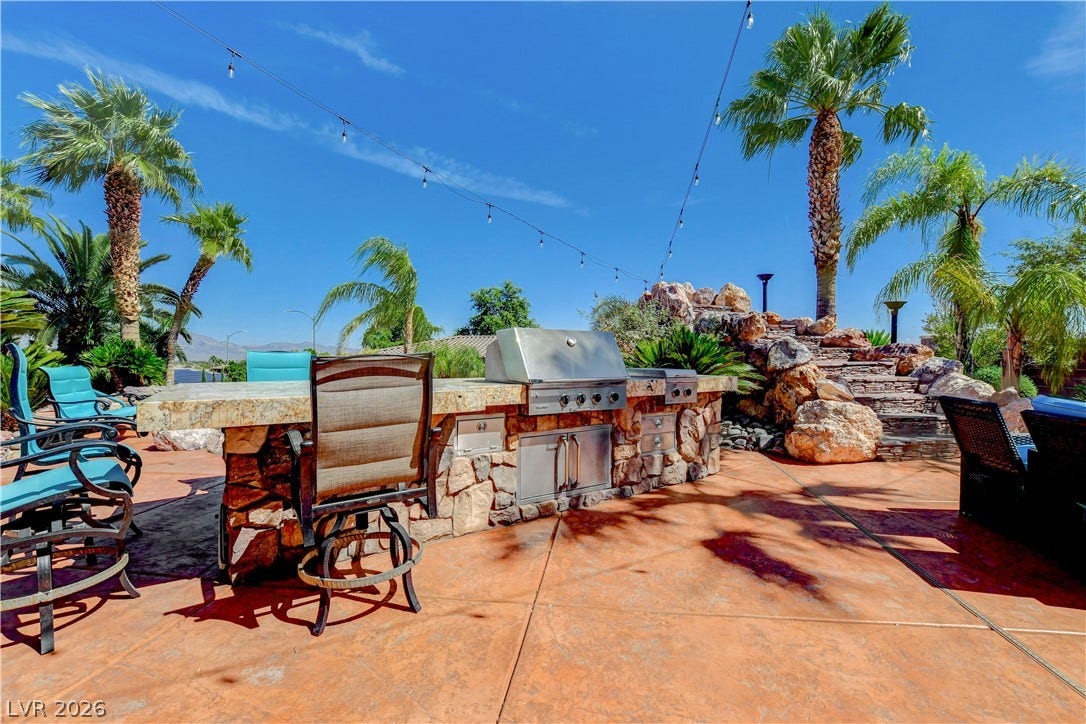 An integrated stone barbecue station crowns a textured concrete patio lined with mature palms.