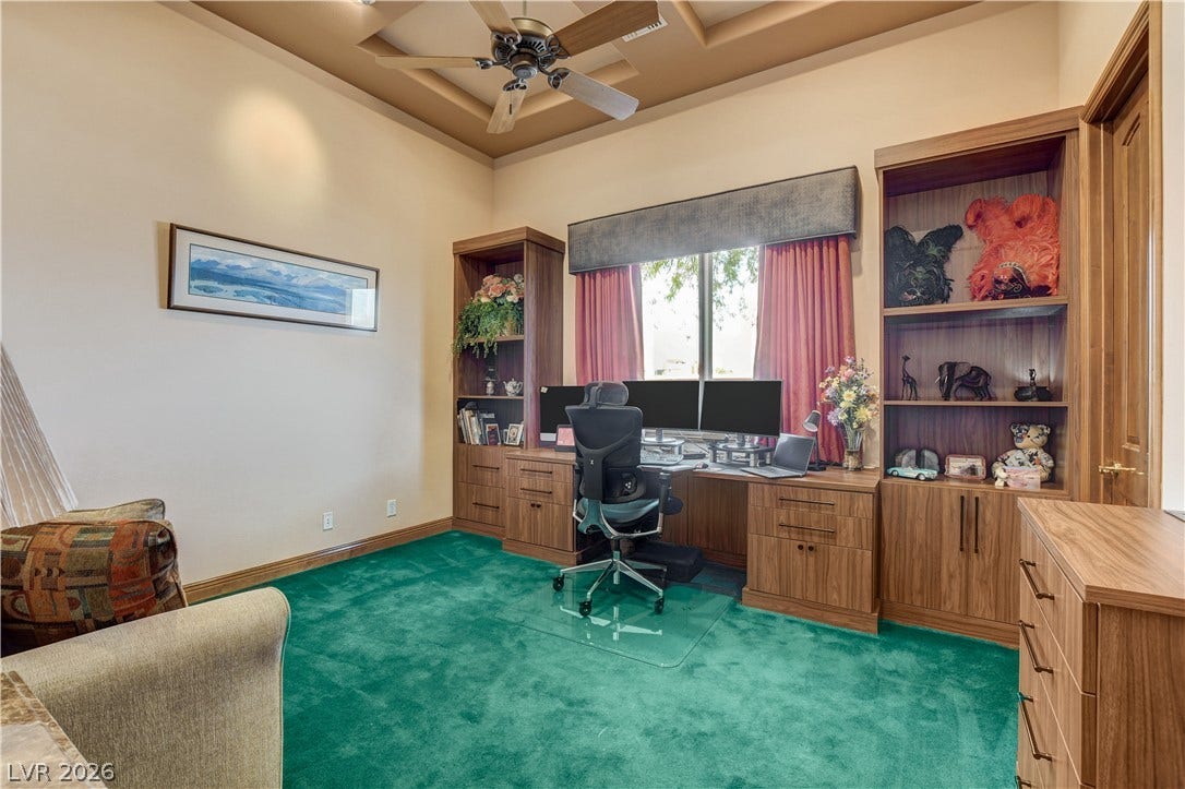 A spacious home workspace includes a tray ceiling and handsome built-in wooden cabinetry.
