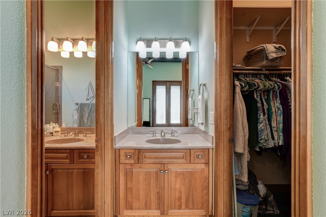 Warm wood cabinetry and stone counters define this master bathroom with an adjacent closet.