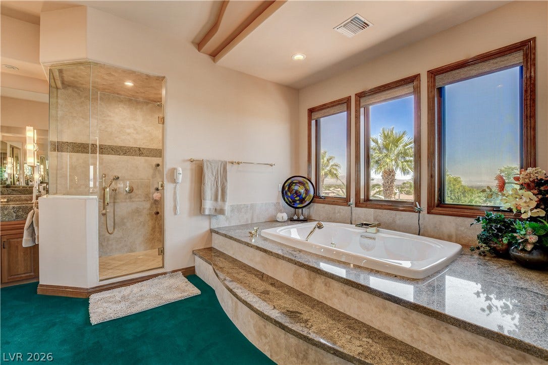An elevated soaking tub sits alongside large wood-framed windows overlooking scenic outdoor palms.