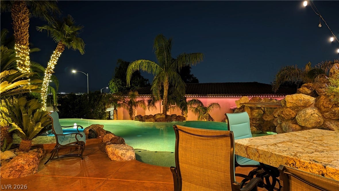 An illuminated swimming pool offers a resort-style backyard experience framed by tropical palms.