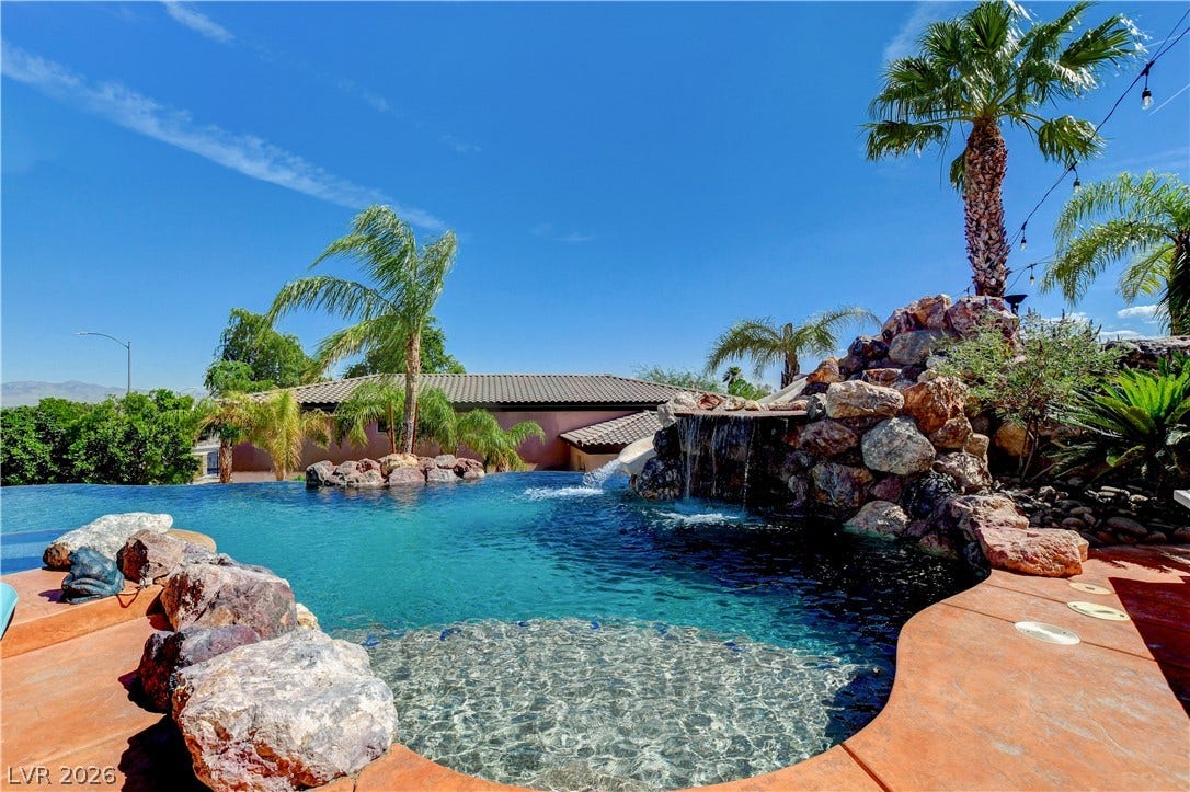 An inviting backyard oasis features a rock waterfall, slide, and towering palm trees.