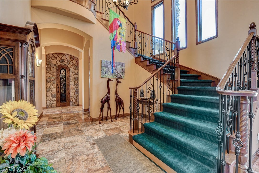 A sweeping staircase with ornate iron railings climbs past tall windows in this grand entryway.