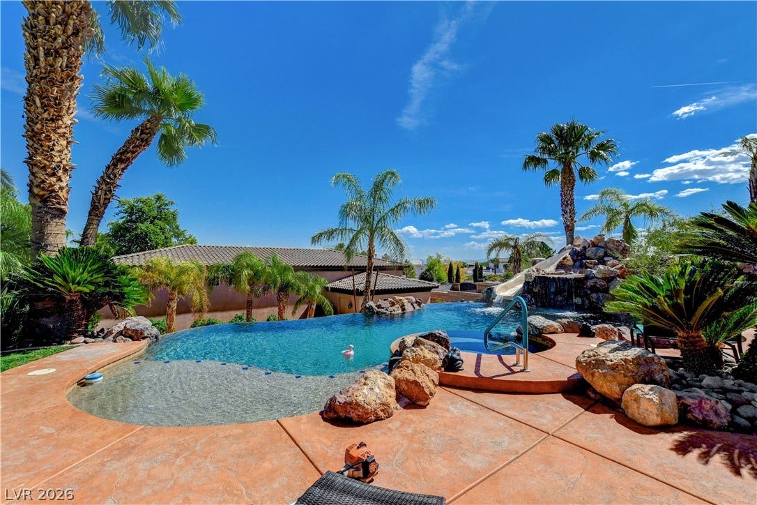 A resort-style swimming pool integrates rock waterfalls and a waterspide amid palm tree landscaping.