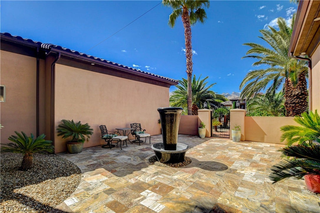 A spacious stone paved courtyard features a central fountain under towering palm trees.