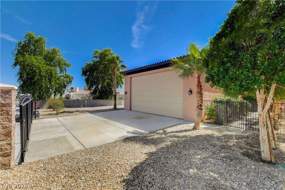 An expansive concrete driveway leads to a spacious two-car garage alongside mature desert landscaping.