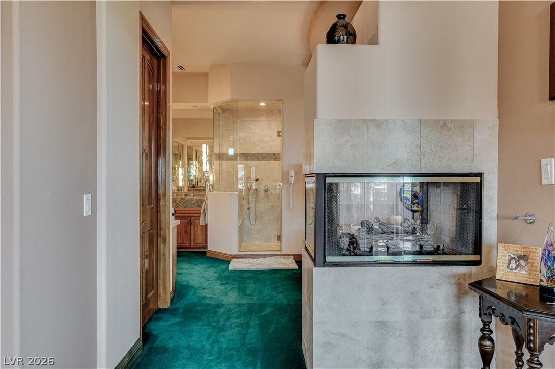 An inviting three-sided fireplace warms the transition into a spacious, light-filled primary bathroom suite.