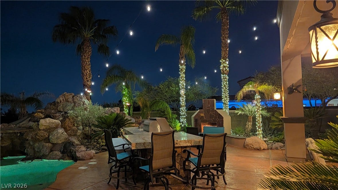 Lush palms and soft lighting frame a stone-accented outdoor entertainment patio beside the pool.