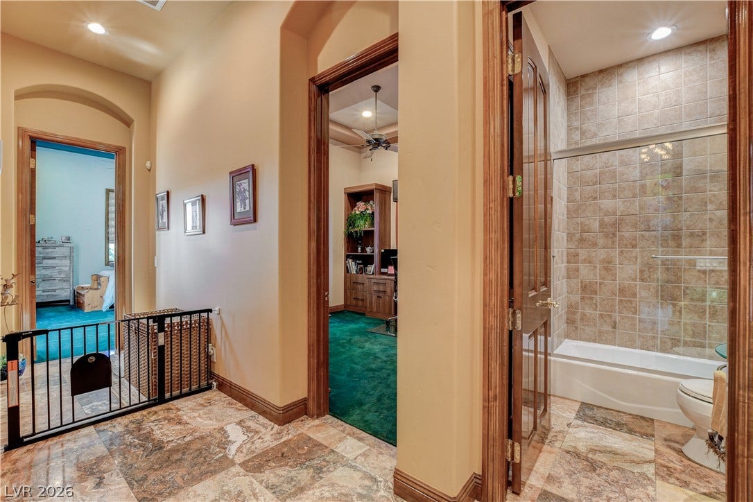 Polished stone flooring and warm wood trim connect the spacious hallway to an adjacent bath.