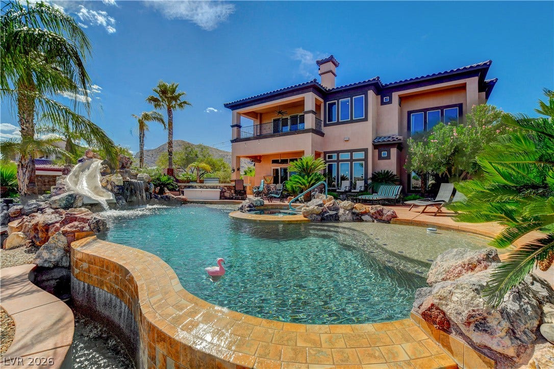An inviting backyard oasis showcases a custom rock waterfall pool set against a multi-level residence.