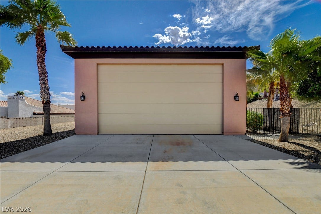 A spacious driveway leads to this detached garage featuring tile roof accents and stucco exterior.