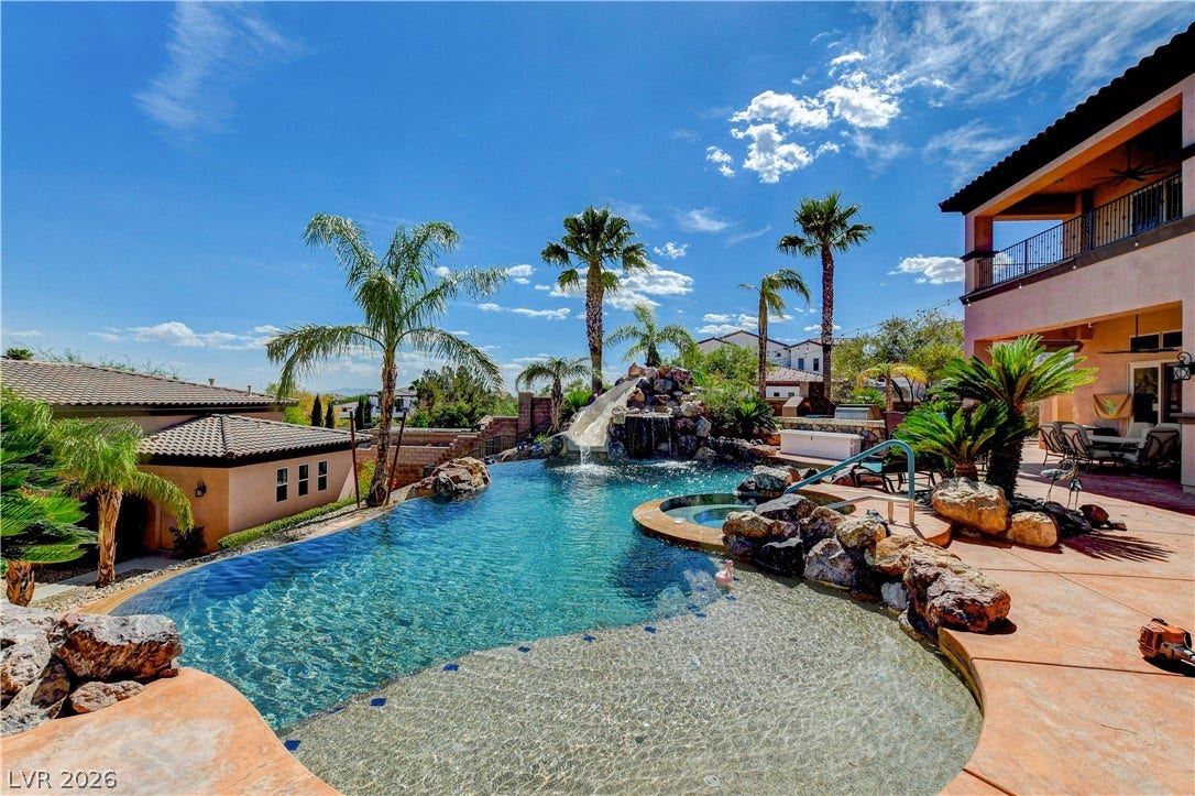 A resort-style swimming pool features a rock waterfall, water slide, and concrete patio surround.