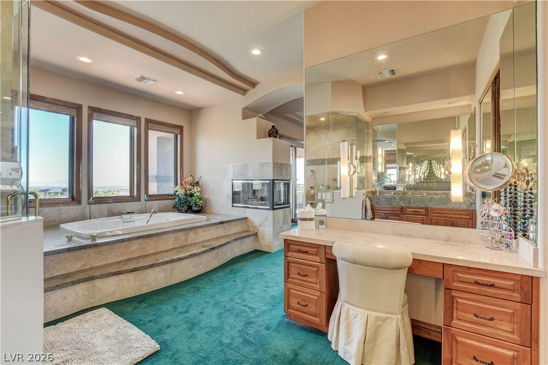 A spacious vanity area sits adjacent to a raised soaking tub framed by windows.