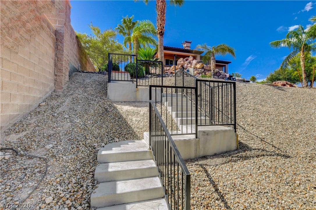 Concrete steps with metal railings lead up a gravel slope framed by palm trees.