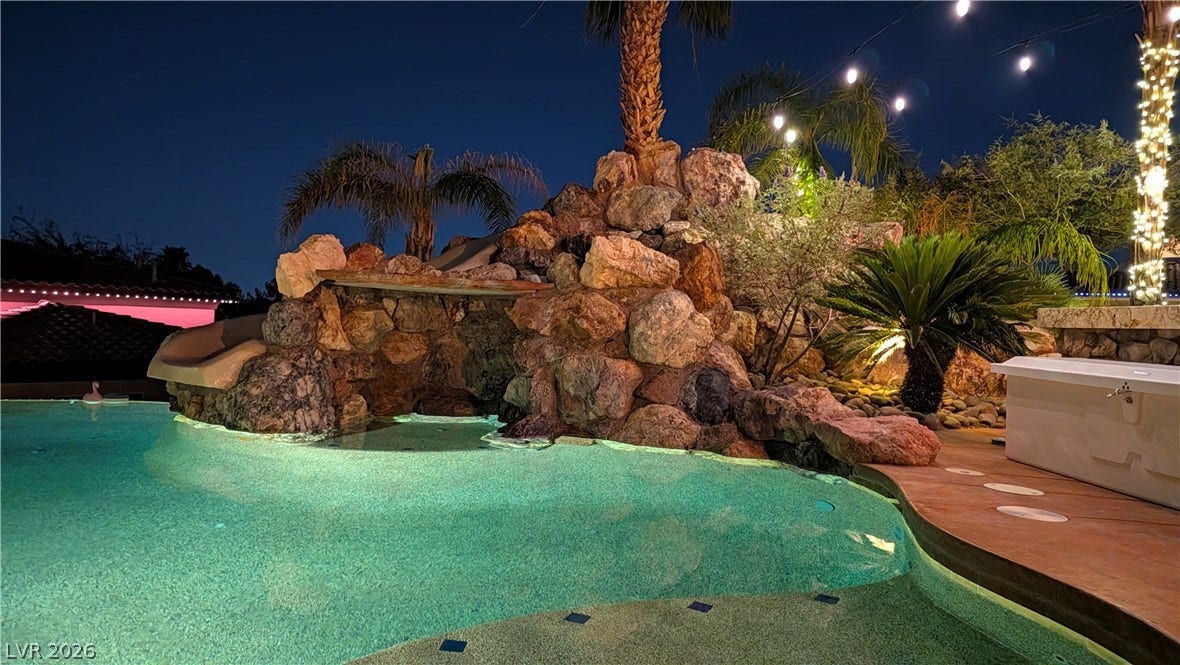 A resort-style swimming pool features a dramatic rock waterfall grotto and a built-in water slide.