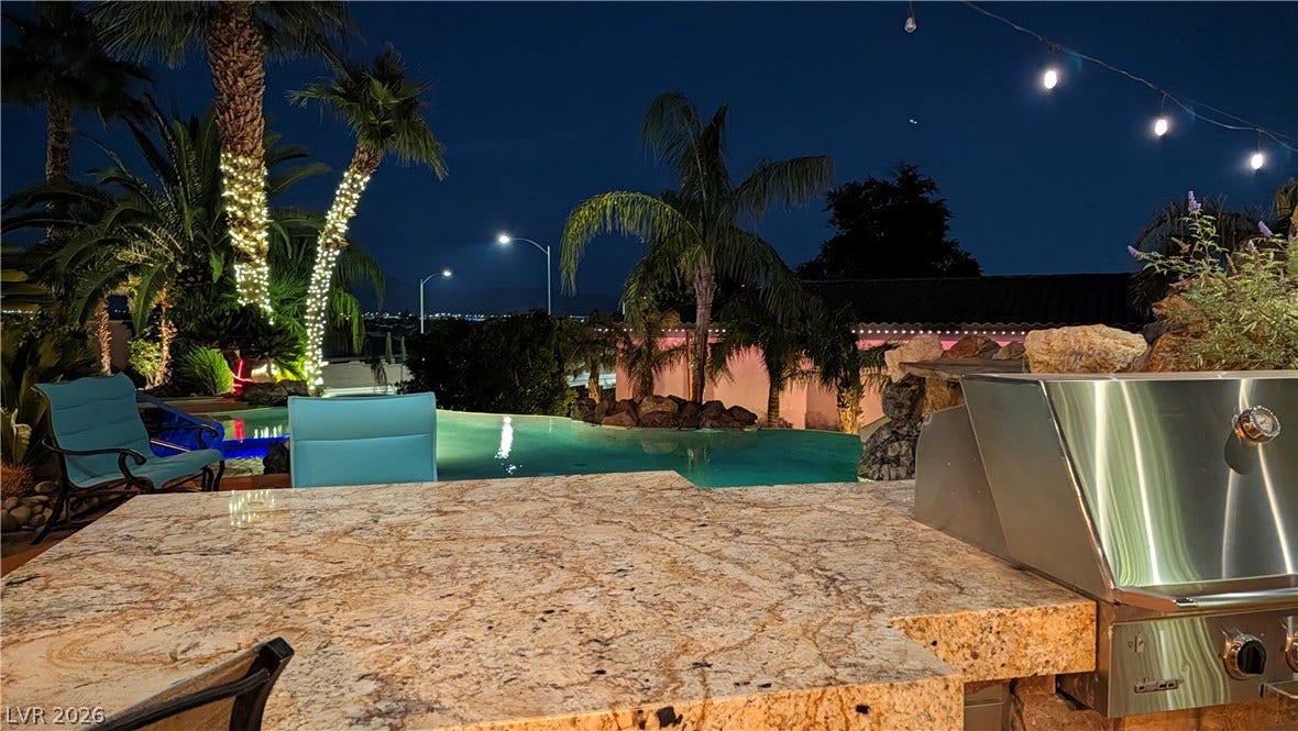 An outdoor kitchen features granite counters alongside a built-in grill overlooking the pool area.