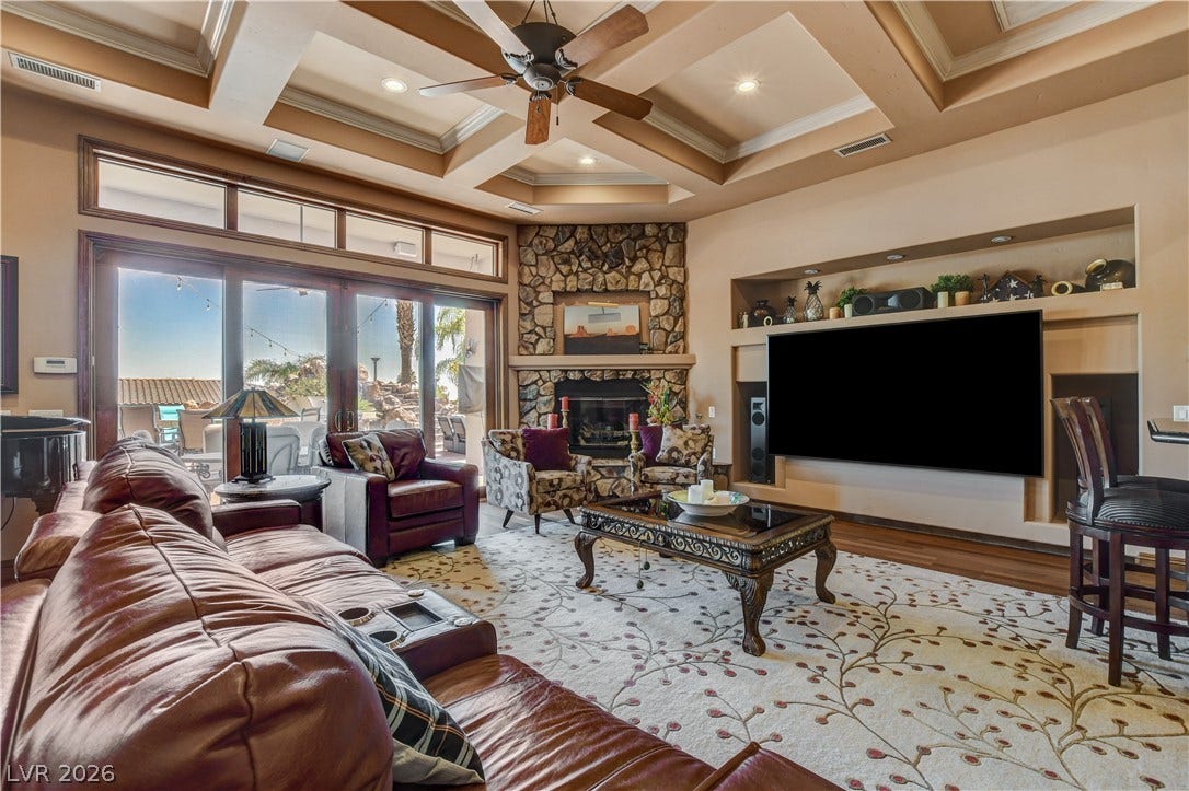 An elegant stone fireplace anchors this living space beneath a dramatic coffered ceiling.