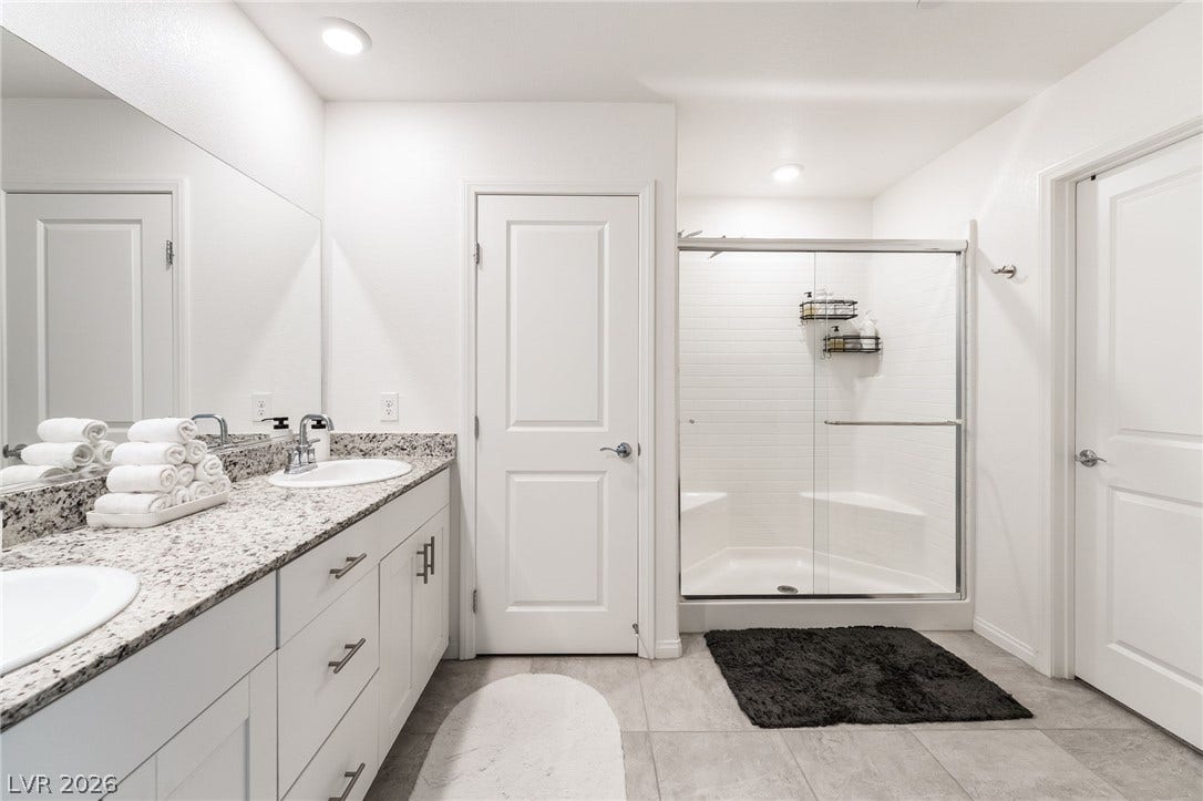 10958 Cheshire Woods Avenue, Las Vegas, NV 89166 A spacious bathroom displays a dual vanity with granite counters and a glass shower enclosure.