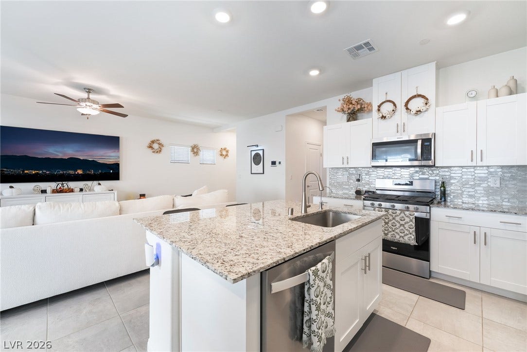 10958 Cheshire Woods Avenue, Las Vegas, NV 89166 Granite countertops and clean white cabinetry highlight an open-concept kitchen seamlessly connected to the living area.