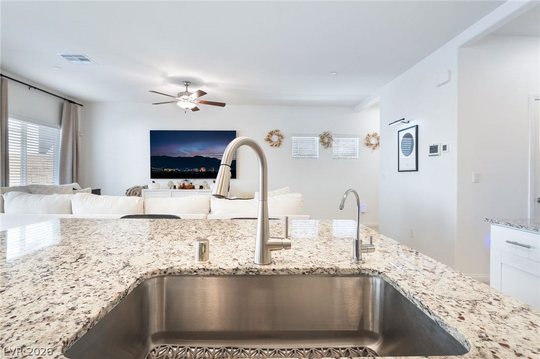 10958 Cheshire Woods Avenue, Las Vegas, NV 89166 Polished granite countertops surround a stainless steel sink overlooking the open-concept living area.