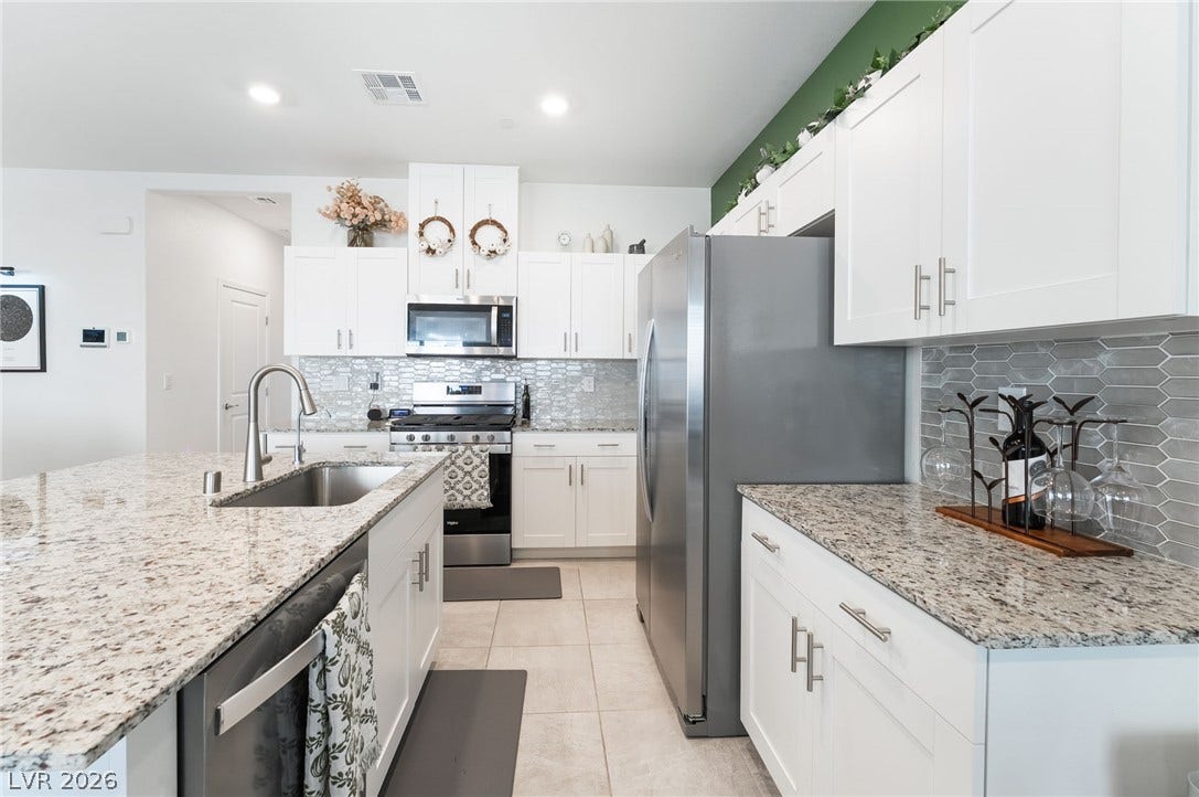 10958 Cheshire Woods Avenue, Las Vegas, NV 89166 Polished granite countertops complement sleek white cabinetry and stainless steel appliances in this modern kitchen.