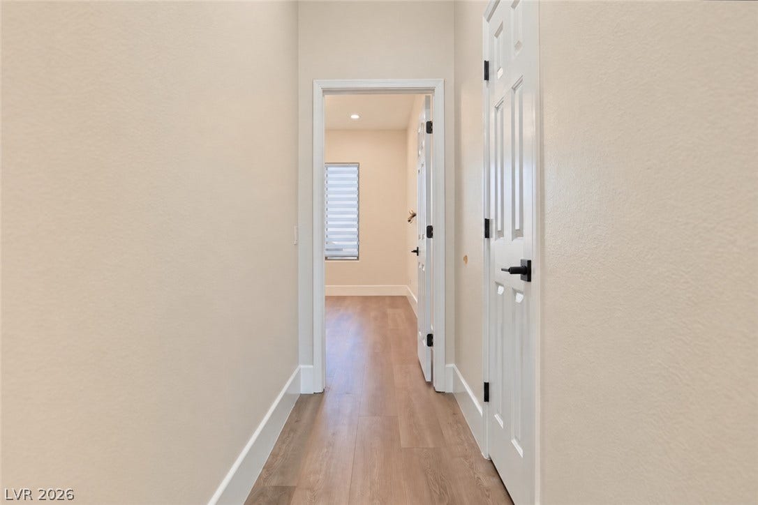 6 Mohansic Road, Henderson, NV 89052 Smooth plaster walls and warm wood-look floors frame a bright, straightforward hallway transition.