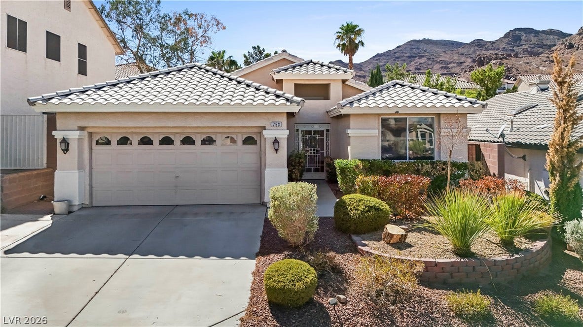 753 Wigan Pier Drive, Henderson, NV 89002 Spanish tile roofing and desert plantings frame this single-story home set against a mountain backdrop.