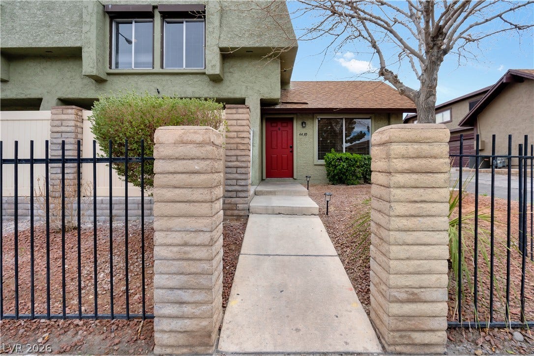 A concrete walkway leads past stone pillars and wrought iron fencing to the front entrance.