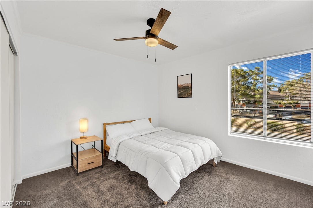 Plush carpeting and a large window framing neighborhood views elevate this peaceful bedroom.