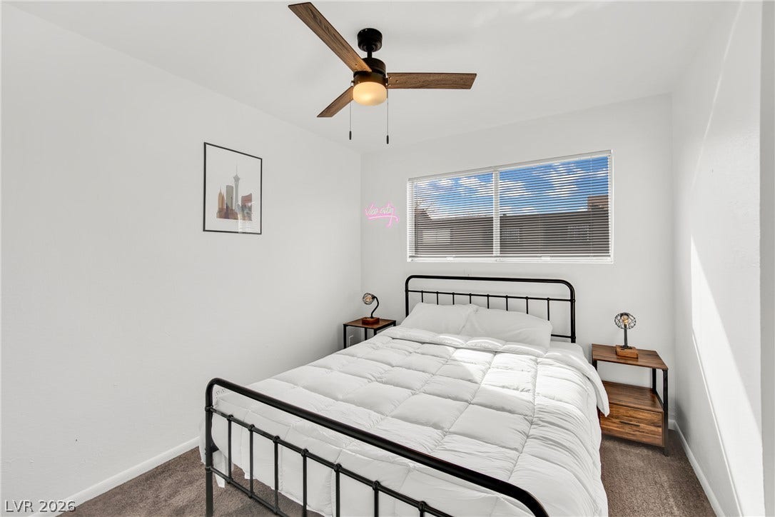 Natural light streams through a wide window in this bedroom featuring plush carpeting.
