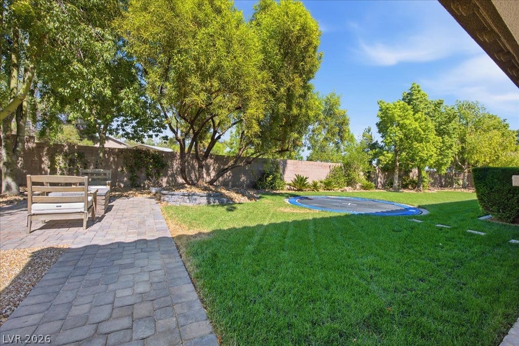 8030 Palm Cove Court, Las Vegas, NV 89129 Mature trees frame a manicured lawn alongside a paved patio in this secluded backyard.